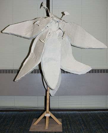 A lilly flower with eyes protruding as stamens and a stem with leaves below the helmet